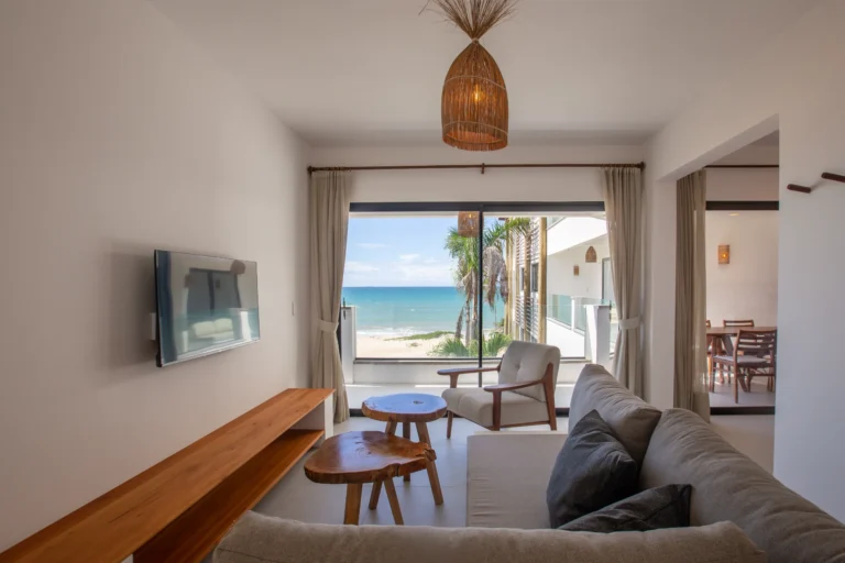 Two-bedroom apartment living room in Cumbuco with a sofa, armchair, wall-mounted TV and sliding doors onto the sea-facing terrace