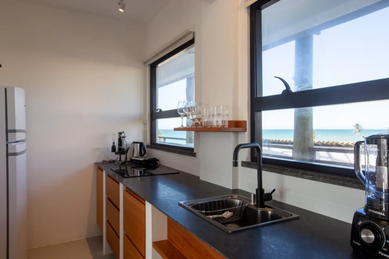 Fully equipped kitchen in a one-bedroom beachfront apartment in Cumbuco, with a dark stone worktop, hob and a window looking out over the ocean