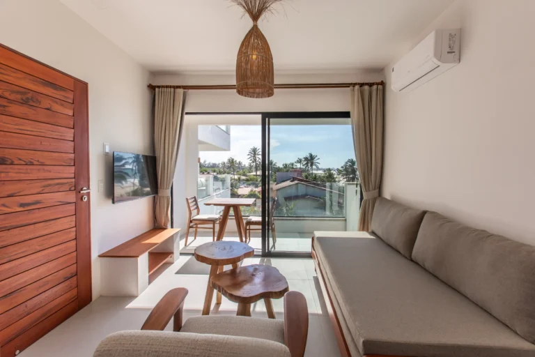 Living area of a one-bedroom apartment at Windtown Cumbuco with a sofa, wall-mounted TV and sliding doors onto the sea-facing terrace