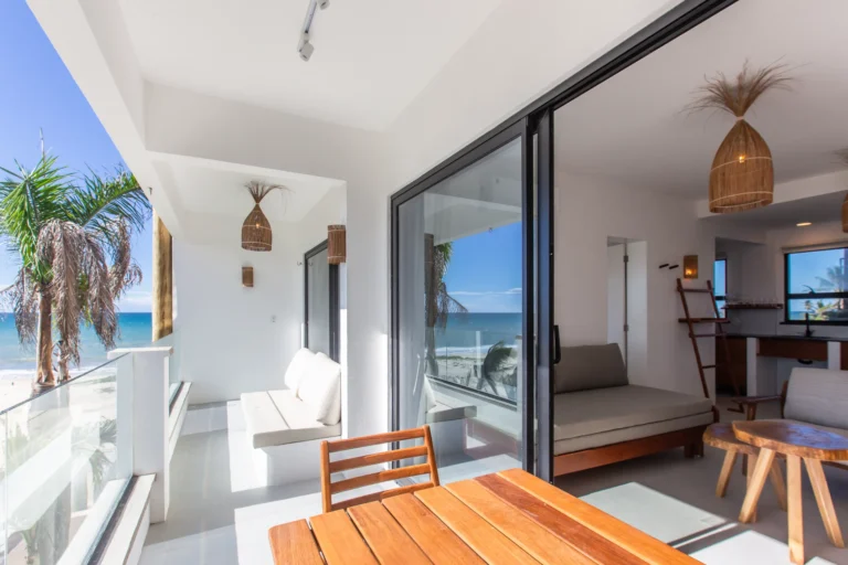 Covered terrace dining table at a one-bedroom apartment at Windtown Cumbuco, looking out over palm trees to the Atlantic