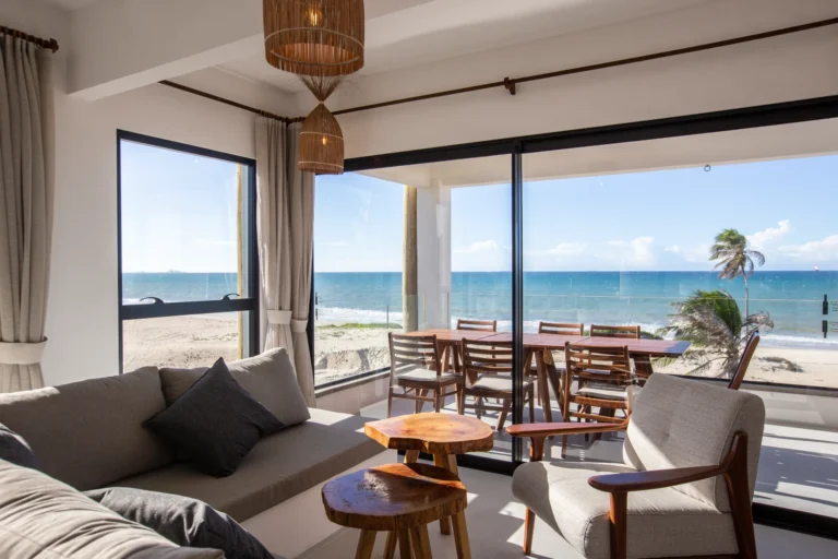 Living and dining area of a three-bedroom apartment in Cumbuco opening onto a terrace with palm trees and a view of the Atlantic