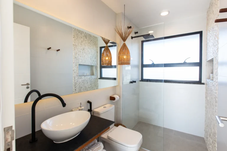 Bathroom in a one-bedroom beachfront apartment in Cumbuco with an oval vessel sink, black fittings and a glass walk-in shower