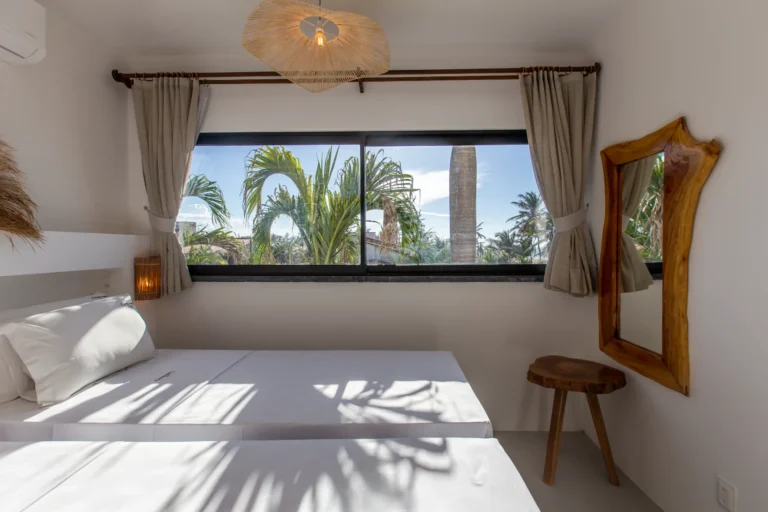 A further bedroom in a three-bedroom beachfront apartment at Windtown Cumbuco, with a wooden mirror and a window onto the palms