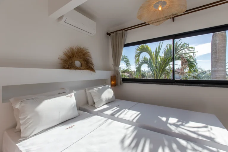 Bright bedroom in a three-bedroom apartment in Cumbuco with palm shadows falling across the bed from a full-height window