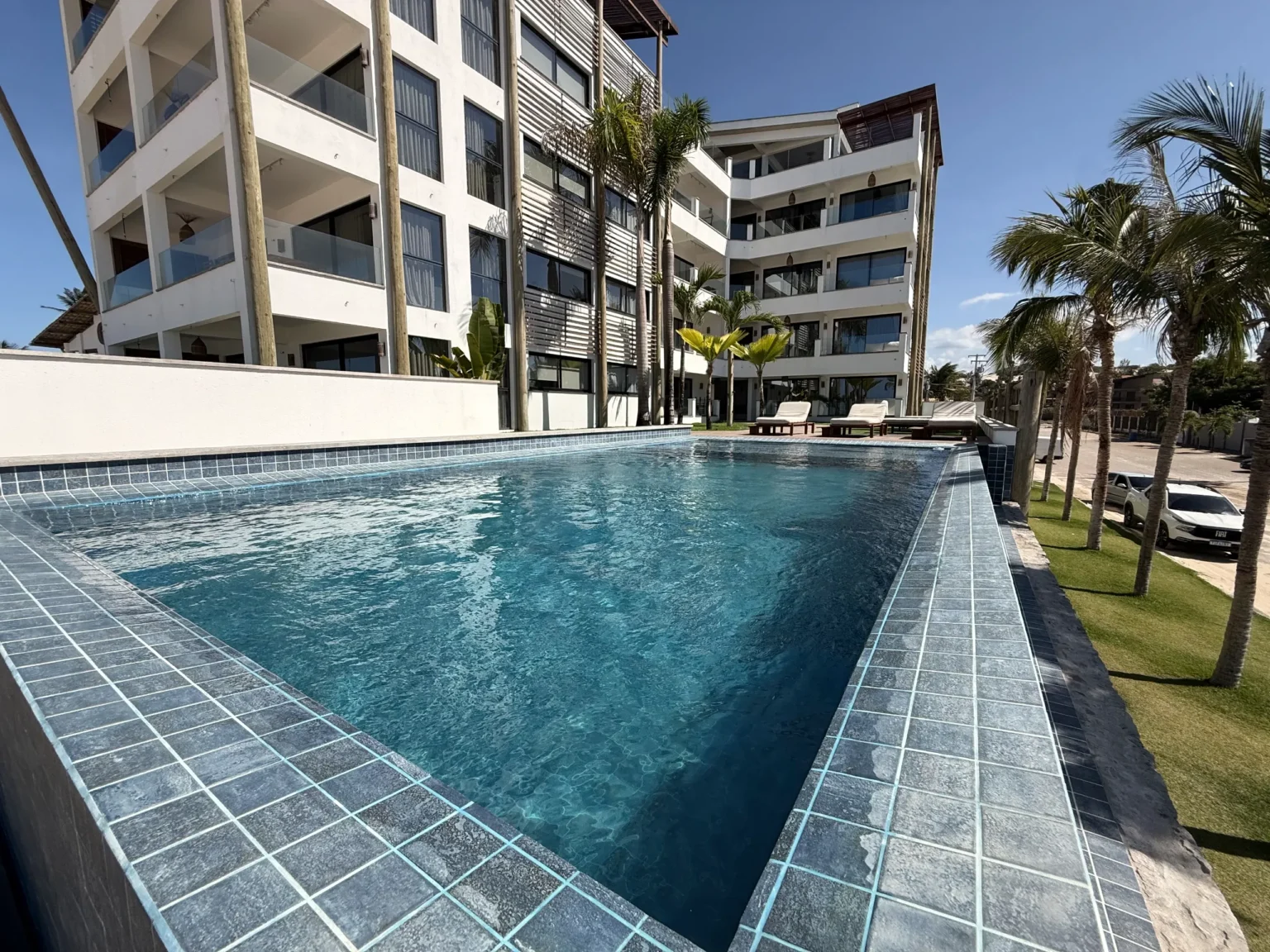 Swimming pool at Windtown Apartments Cumbuco, lined with teak loungers and palm trees beside the apartment building