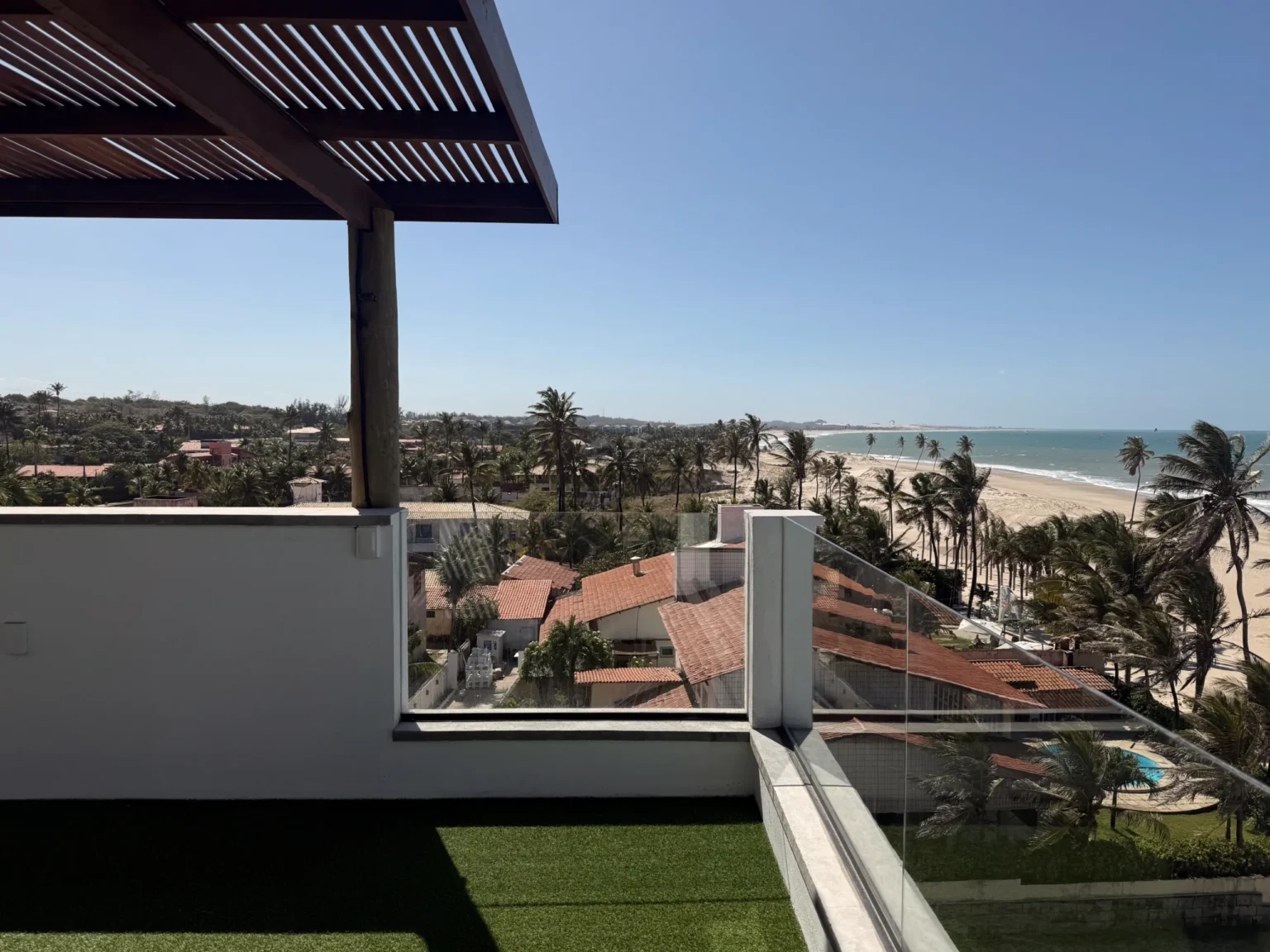Shared roof terrace at Windtown Apartments in Cumbuco, with a shaded pergola and a panoramic view over the village rooftops to the Atlantic